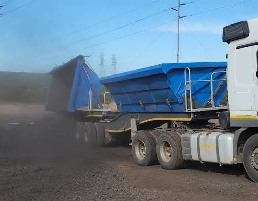 Blue side-tipper trailer hauling material on a dirt road